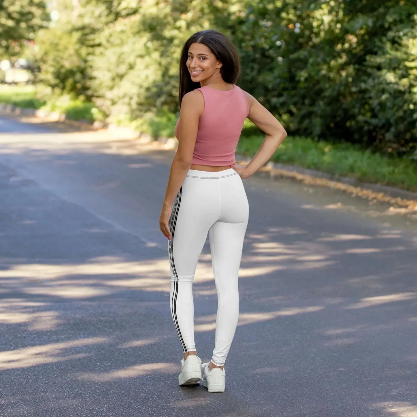 Woman smiling in white leggings with black stripes and pink sleeveless top on sunny outdoor path